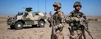 Soldaten der Bundeswehr sichern die Umgebung während eine Übung in Afghanistan. Zwei Soldaten stehen nebeneinander und beobachten die Umgebung, im Hintergrund steht ein Fahrzeug vom Typ Dingo