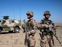 Soldaten der Bundeswehr sichern die Umgebung während eine Übung in Afghanistan. Zwei Soldaten stehen nebeneinander und beobachten die Umgebung, im Hintergrund steht ein Fahrzeug vom Typ Dingo