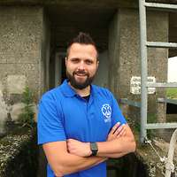 A man standing in front of a building with a thick steel door with his arms crossed.