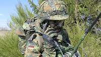 Ein Soldat mit Helm und Tarnschminke hält den Hörer eines Funkgerätes ans Ohr.