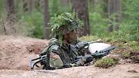 Ein bewaffneter Soldat mit getarntem Helm steht in einer ausgehobenen Stellung.