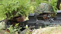 Zwei Soldaten mit getarnten Helmen liegen mit Gewehren im Anschlag und schauen durchs Zielfernrohr.
