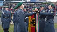 Sechs Soldaten haben eine Hand auf die Truppenfahne gelegt, die ein siebter waagerecht hält.