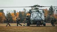 Fünf Fallschirmjägersoldaten verlassen mit ihren Waffen und Gepäck einen Transporthubschrauber.