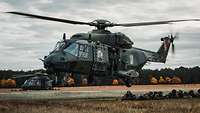 Ein Militärhubschrauber hebt ab, unter ihm die soeben abgesetzten Soldaten, die auf dem Boden liegen.
