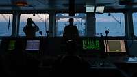 Soldaten der Bundeswehr in Rückenansicht stehen auf der Brücke eines Schiffes bei Dämmerung und schauen auf das offene Meer