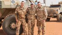 Drei Soldaten stehen an einem Radpanzer