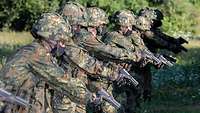 Mehrere Soldaten in Flecktarn und Schießanzug stehen nebeneinander, in der Hand halten sie eine Pistole auf Boden gerichtet.