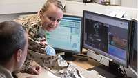Eine deutsche Soldatin im Gespräch mit einem rumänischen Soldaten, vor ihnen drei Computerbildschirme mit Wetterdaten