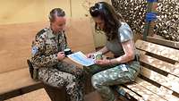 Eine rumänische und eine deutsche Soldatin sitzen sich im Gespräch gegenüber und blicken auf ein DIN-A4-Blatt