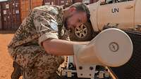 Ein Soldat stellt einen Störsender ein, im Hintergrund ein Fahrzeug der UN und mehrere Container 