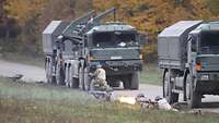 Ungarische Soldaten im Feuergefecht, vor allem im Liegendanschlag, vor abgestellten Lastwagen.