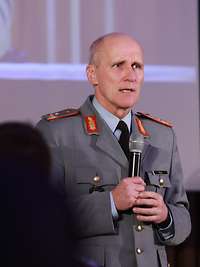 Generalmajor Oliver Kohl begrüßt mit einem Mikrofon in der Hand die analogen und digitalen Gäste des Innovationslabors