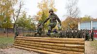 Zwei Soldaten auf der Hindernisbahn, weitere Soldaten sehen im Hintergrund zu