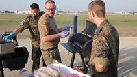 Soldaten stehen vor einem Smoker und bereiten Essen für die anderen Kameradinnen und Kameraden vor.