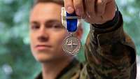 Ein Soldat hält eine silberne Medalie hoch