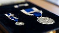 Eine kleine und eine große silberne Medalie mit Nato Symbol in einer Schachtel