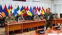 Mehrere Soldaten verschieder Nationen sitzen vor veschiedenen Flaggen