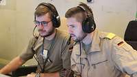 Zwei Soldaten mit Headset sitzen vor einem Rechner