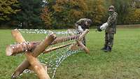 Auf einer Wiese stehen zwei Andreaskreuze aus Rundhölzern, die mit einem langen Riegel verbunden sind. 