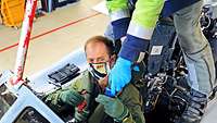 Ein Pilot wird im Flugzeug von einem Mann angeschnallt