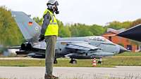 Ein Soldat mit Maske und Helm steht auf dem Flugfeld und guckt