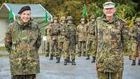 Zwei Soldaten stehen nebeneinander, im Hintergrund sind weitere Soldaten angetreten.