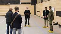 Fünf männliche Personen, darunter eine in Uniform, stehen in einer Sporthalle