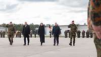 Zwei Soldaten und drei Zivilisten schreiten nebeneinander die angetretene Formation der Soldat ab.