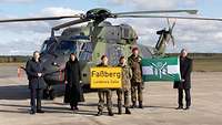 Gruppenfoto vor einem Hubschrauber mit Ortsschild und Flagge.