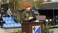 Ein Soldat hält eine Rede vor weiteren Soldaten und Zivilisten.