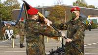 Ein Soldat überreicht einem anderen Soldaten eine Truppenfahne.