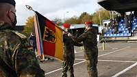 Ein Soldat überreicht einem anderen Soldaten eine Truppenfahne.