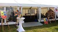 Ein großes Zelt, davor ein Wappen, ein Glücksrad und ein Bistrotisch