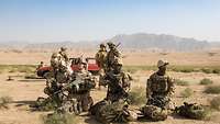 Vier Soldaten sind kniend im Vordergrund. Im Mittelgrund stehen drei weitere Soldaten. Dahinter steht ein Auto