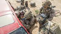 Zwei Soldaten ziehen einen weiteren aus einem Auto. Zwei andere stehen daneben und beobachten die Situation