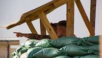 Zwei Soldaten stehen hinter Sandsäcken unter einem Holzdach.