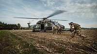 Soldaten tragen einen verwundeten Kameraden zum Huschrauber, der auf dem Feld steht