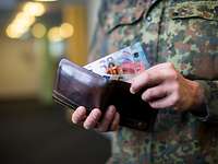 Grundgehälter von Soldaten und Beamten: Wer verdient wieviel? Ein Bundeswehrsoldat steckt mehrere Geldscheine in ein Portemonnaie