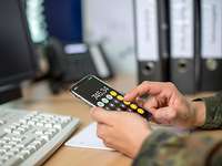 Gehalt neu berechnen: Finanzielle Zulagen für Soldaten. Ein Bundeswehrsoldat sitzt an einem Schreibtisch und rechnet mit einem Mobiltelefon