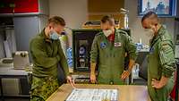 Zwei deutsche Piloten und ein estnischer JTAC stehen um einen Tisch herum und tauschen sich aus.