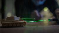 Ein Plastikmodel eines Kampfpanzers wird mit einen grünen Laserpointer angestrahlt.