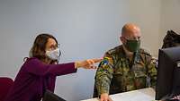 Ein Soldat mit Mundschutz und eine Frau mit Maske sitzen vor einem PC-Bildschirm. Sie zeigt auf den Bildschirm.