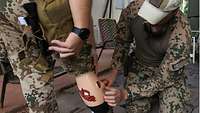 Ein Soldat legt einem anderen Soldaten eine Moulage ans Bein an
