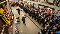 Mehrere Soldaten in blauer Arbeitsuniform stehen nebeneinader im Hangar eines Kriegsschiffs.