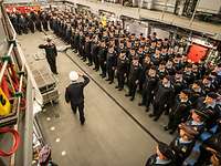 Mehrbesatzungsmodell Mehrere Soldaten in blauer Arbeitsuniform stehen nebeneinader im Hangar eines Kriegsschiffs.