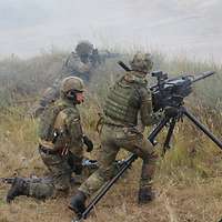 Drei Soldaten befinden sich mit der aufgebauten Granatmaschinenwaffe in einer Stellung.