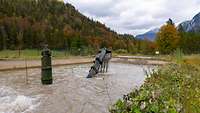 Aus einem Wasserbecken schaut eine Röhre in der ein Soldat steht und ein Baggerarm mit Kies in der Schaufel