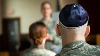 Ein amerikanischer Soldat mit Kippa im Vordergrund sitzt mit einer Kameradin vor einer amerikanischen Militärrabbinerin