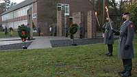 Mehrere Soldaten stehen mit Fackeln in der Hand an einer Gedenkstätte. Auf Metallständern hängen Kränze.